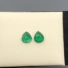 Studio close-up photographs displaying a matched pair of pear-shaped natural green emerald gemstones resting side-by-side inside an open black presentation box.