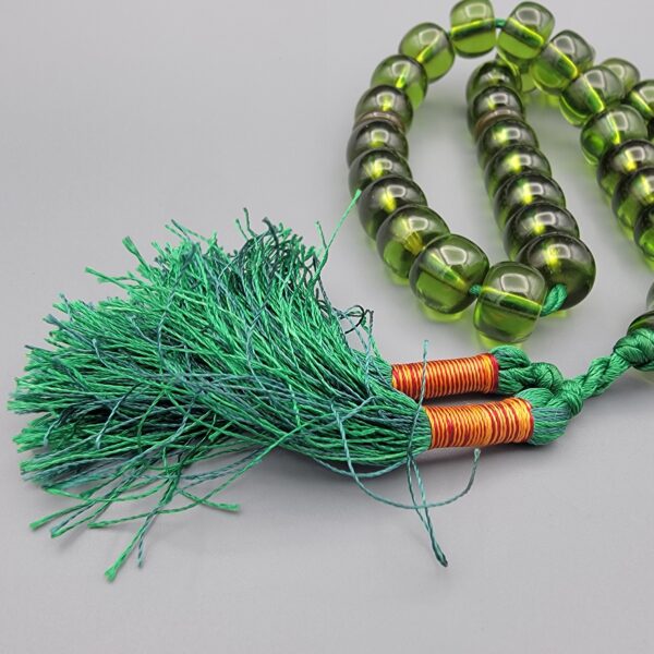 Studio close-up photograph of a 98-gram olive-green German Bakelite Sandaloos tasbih rosary, featuring barrel-cut polished beads, an intricately sculpted imam bead, and a rich green tassel against a light background.
