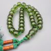 Studio close-up photograph of a 98-gram olive-green German Bakelite Sandaloos tasbih rosary, featuring barrel-cut polished beads, an intricately sculpted imam bead, and a rich green tassel against a light background.