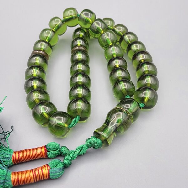 Studio close-up photograph of a 98-gram olive-green German Bakelite Sandaloos tasbih rosary, featuring barrel-cut polished beads, an intricately sculpted imam bead, and a rich green tassel against a light background.