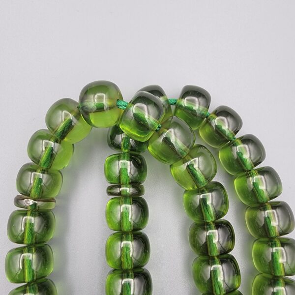 Studio close-up photograph of a 98-gram olive-green German Bakelite Sandaloos tasbih rosary, featuring barrel-cut polished beads, an intricately sculpted imam bead, and a rich green tassel against a light background.