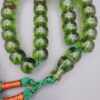 Studio close-up photograph of a 98-gram olive-green German Bakelite Sandaloos tasbih rosary, featuring barrel-cut polished beads, an intricately sculpted imam bead, and a rich green tassel against a light background.
