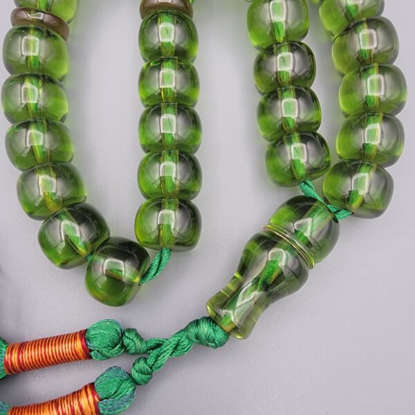 Studio close-up photograph of a 98-gram olive-green German Bakelite Sandaloos tasbih rosary, featuring barrel-cut polished beads, an intricately sculpted imam bead, and a rich green tassel against a light background.