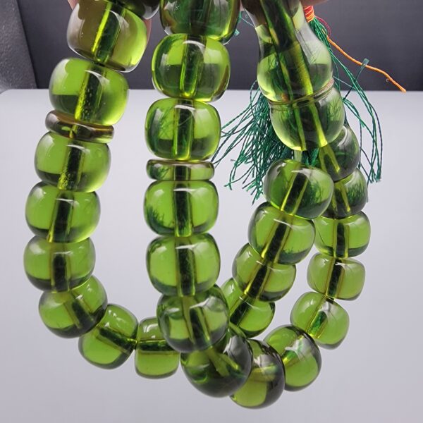 Studio close-up photograph of a 98-gram olive-green German Bakelite Sandaloos tasbih rosary, featuring barrel-cut polished beads, an intricately sculpted imam bead, and a rich green tassel against a light background.