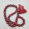 Studio close-up photograph of a 60-gram deep red German Bakelite Sandaloos tasbih rosary, featuring barrel-cut polished beads, an intricately sculpted imam bead, and a rich red cord tassel against a light background.