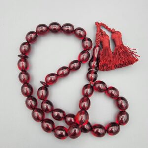 Studio close-up photograph of a 60-gram deep red German Bakelite Sandaloos tasbih rosary, featuring barrel-cut polished beads, an intricately sculpted imam bead, and a rich red cord tassel against a light background.