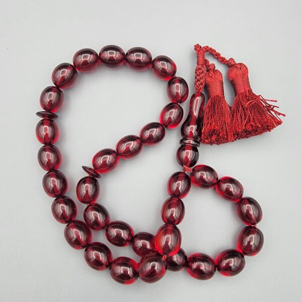 Studio close-up photograph of a 60-gram deep red German Bakelite Sandaloos tasbih rosary, featuring barrel-cut polished beads, an intricately sculpted imam bead, and a rich red cord tassel against a light background.