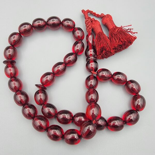 Studio close-up photograph of a 60-gram deep red German Bakelite Sandaloos tasbih rosary, featuring barrel-cut polished beads, an intricately sculpted imam bead, and a rich red cord tassel against a light background.