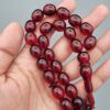 Studio close-up photograph of a 60-gram deep red German Bakelite Sandaloos tasbih rosary, featuring barrel-cut polished beads, an intricately sculpted imam bead, and a rich red cord tassel against a light background.