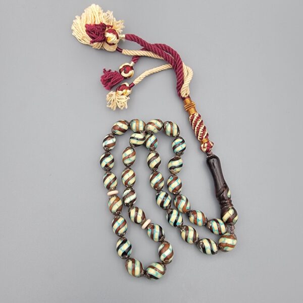 Studio close-up photograph of a 39-gram natural Yusr coral retro swirl striped composite tasbih prayer bead strand, featuring barrel-cut beads with turquoise-blue, maroon, and cream accents, a matching imam bead, and a multi-colored tassel against a light grey background.