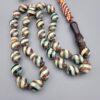 Studio close-up photograph of a 39-gram natural Yusr coral retro swirl striped composite tasbih prayer bead strand, featuring barrel-cut beads with turquoise-blue, maroon, and cream accents, a matching imam bead, and a multi-colored tassel against a light grey background.