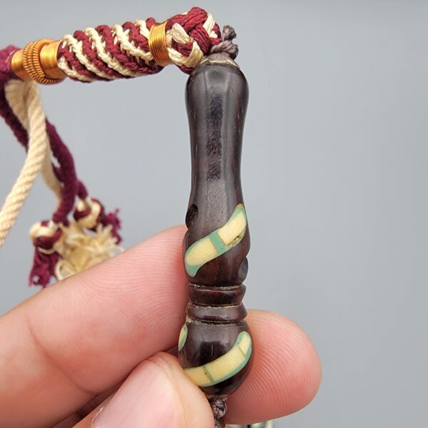 Studio close-up photograph of a 39-gram natural Yusr coral retro swirl striped composite tasbih prayer bead strand, featuring barrel-cut beads with turquoise-blue, maroon, and cream accents, a matching imam bead, and a multi-colored tassel against a light grey background.