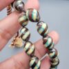 Studio close-up photograph of a 39-gram natural Yusr coral retro swirl striped composite tasbih prayer bead strand, featuring barrel-cut beads with turquoise-blue, maroon, and cream accents, a matching imam bead, and a multi-colored tassel against a light grey background.