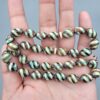 Studio close-up photograph of a 39-gram natural Yusr coral retro swirl striped composite tasbih prayer bead strand, featuring barrel-cut beads with turquoise-blue, maroon, and cream accents, a matching imam bead, and a multi-colored tassel against a light grey background.