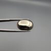 Studio close-up photographs displaying an 18.82-carat oval-cut natural brassy-gold pyrite gemstone with a metallic luster, held securely in precision tweezers against a neutral grey background.