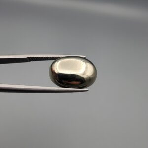 Studio close-up photographs displaying an 18.82-carat oval-cut natural brassy-gold pyrite gemstone with a metallic luster, held securely in precision tweezers against a neutral grey background.