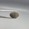 Studio close-up photographs displaying an 18.82-carat oval-cut natural brassy-gold pyrite gemstone with a metallic luster, held securely in precision tweezers against a neutral grey background.