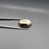 Studio close-up photographs showcasing a 16.38-carat oval-cut natural brassy-gold pyrite gemstone with a metallic luster, held securely in precision tweezers against a neutral grey background.