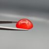 Studio close-up photographs displaying a 20.02-carat oval-cut natural radiant ember orangish-red agate Aqeeq gemstone, held securely in precision tweezers against a neutral grey background.