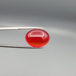 Studio close-up photographs displaying a 22.74-carat oval-cut natural crimson drop brilliant polished red agate Aqeeq gemstone, held securely in precision tweezers against a neutral grey background.
