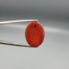 Studio close-up photograph showcasing a 22.63-carat natural carnelian agate Aqeeq cabochon with unique visible dark inclusions, held securely in precision tweezers against a neutral background.