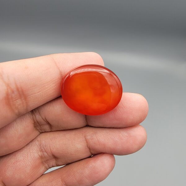 ​Studio close-up photographs displaying a 35.21-carat oval-cut natural nebula glow carnelian agate gemstone featuring unique white crystalline plumes, held securely in precision tweezers against a neutral background.