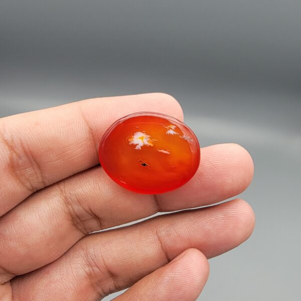 ​Studio close-up photographs displaying a 35.21-carat oval-cut natural nebula glow carnelian agate gemstone featuring unique white crystalline plumes, held securely in precision tweezers against a neutral background.