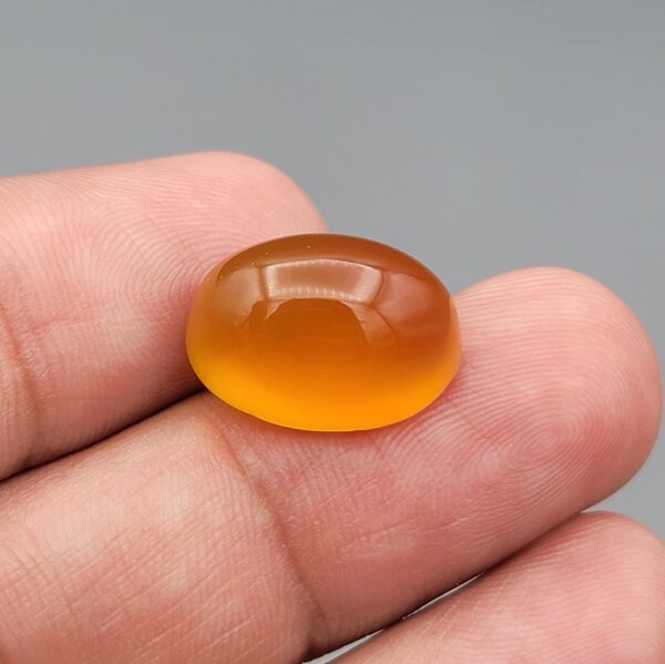 Close-up photograph showcasing a 13.70-carat natural amber drop carnelian high-dome oval cabochon gemstone resting gracefully on an open hand.