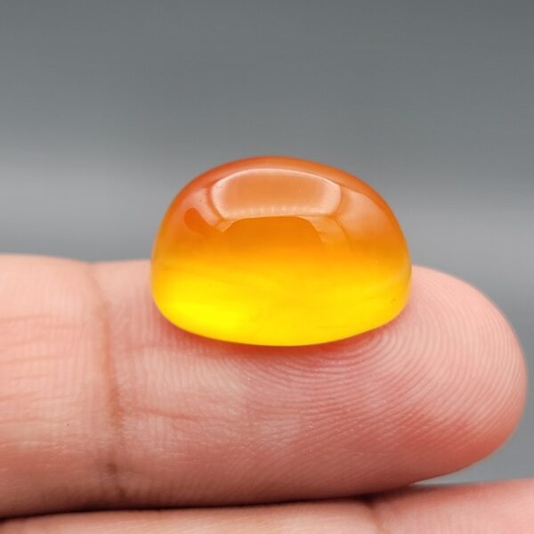 Close-up photograph showcasing a 14.38-carat natural honey drop carnelian high-dome oval cabochon gemstone resting gracefully on an open hand.