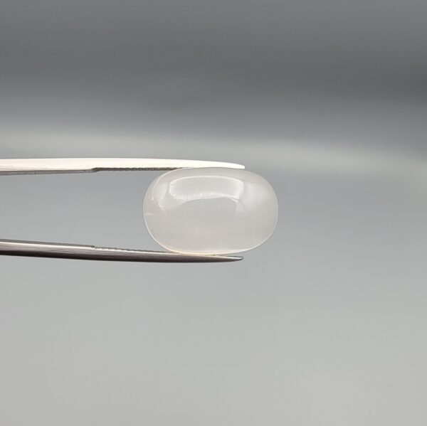 Studio close-up photograph displaying a 15.94-carat natural Durr-e-Najaf oval cabochon gemstone of spiritual purity held securely in precision tweezers against a neutral grey background.