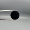 Close-up photograph of a 13.72-carat natural black eye agate cabochon gemstone held in stainless steel tweezers against a neutral grey background, featuring a distinct concentric white ring eye pattern on a polished black surface.