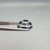 Close-up photograph of a 7.89-carat natural black eye agate cabochon gemstone held in stainless steel tweezers against a neutral grey background, featuring distinct concentric white eye rings and linear banding on a polished black surface.