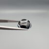 Close-up photograph of a 7.89-carat natural black eye agate cabochon gemstone held in stainless steel tweezers against a neutral grey background, featuring distinct concentric white eye rings and linear banding on a polished black surface.
