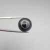 Close-up photograph of a 12.75-carat natural black eye agate cabochon gemstone held in stainless steel tweezers against a neutral grey background, showcasing a prominent concentric white eye pattern set against an intense black center and a patterned translucent greyish-blue reverse.