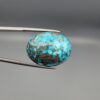 Close-up photograph of a 45.95-carat natural robin's-egg blue Persian turquoise oval cabochon held in stainless steel tweezers against a neutral background, highlighting its vibrant blue tone, heavy metallic pyrite patches, and organic matrix backing.