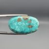 Close-up photograph of a 44.26-carat natural bright sky-blue Persian turquoise oval cabochon held in stainless steel tweezers against a neutral grey background, showcasing vibrant sky-blue saturation and distinct metallic pyrite patches.
