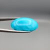 Two-part macro photograph of a 46.42-carat natural blue Sleeping Beauty turquoise (Razaki Feroza) oval cabochon held in tweezers, featuring a high-gloss, flawless sky-blue front face and a reverse side displaying a pale fibrous host matrix.