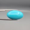 Two-part macro photograph of an 18.01-carat natural bright blue Sleeping Beauty turquoise (Razaki Feroza) oval cabochon held in tweezers, showcasing a vibrant, uniform polished front face and a reverse side with a delicate branching white host matrix pattern.
