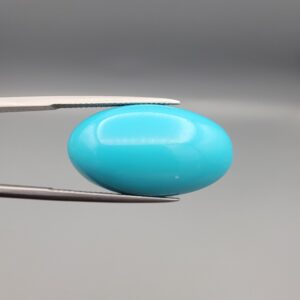 Two-part macro photograph of an 18.01-carat natural bright blue Sleeping Beauty turquoise (Razaki Feroza) oval cabochon held in tweezers, showcasing a vibrant, uniform polished front face and a reverse side with a delicate branching white host matrix pattern.