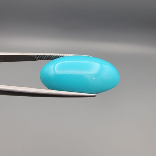 Two-part macro photograph of an 18.01-carat natural bright blue Sleeping Beauty turquoise (Razaki Feroza) oval cabochon held in tweezers, showcasing a vibrant, uniform polished front face and a reverse side with a delicate branching white host matrix pattern.