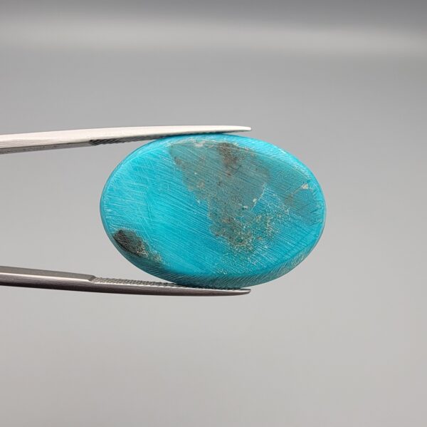 Multi-angle macro photographs of a 32-carat natural vibrant sky-blue Sleeping Beauty turquoise (Razaki Feroza) oval cabochon held in tweezers, featuring a smooth domed front face with subtle natural variations and a reverse side displaying an authentic dark matrix.