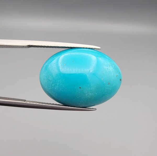 Multi-angle macro photographs of a 20.57-carat natural vibrant sky-blue Sleeping Beauty turquoise (Razaki Feroza) oval cabochon held in tweezers, showcasing a brilliantly polished front face and a reverse surface densely patterned with dark, mottled matrix inclusions.