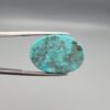 Multi-angle macro photographs of a 20.57-carat natural vibrant sky-blue Sleeping Beauty turquoise (Razaki Feroza) oval cabochon held in tweezers, showcasing a brilliantly polished front face and a reverse surface densely patterned with dark, mottled matrix inclusions.