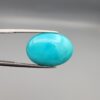 Multi-angle macro photographs of a 12.89-carat natural vibrant sky-blue Sleeping Beauty turquoise (Razaki Feroza) oval cabochon held in tweezers, featuring a brilliant polished front face and a reverse surface displaying an intricate greenish-grey and white host matrix.