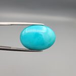 Multi-angle macro photographs of a 12.89-carat natural vibrant sky-blue Sleeping Beauty turquoise (Razaki Feroza) oval cabochon held in tweezers, featuring a brilliant polished front face and a reverse surface displaying an intricate greenish-grey and white host matrix.
