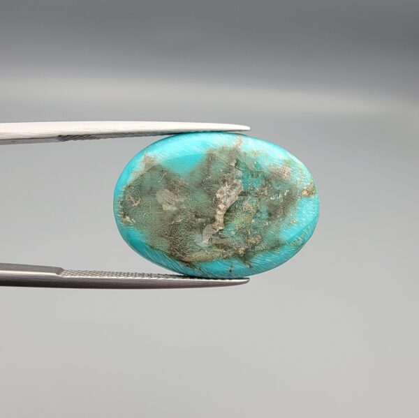 Multi-angle macro photographs of a 12.89-carat natural vibrant sky-blue Sleeping Beauty turquoise (Razaki Feroza) oval cabochon held in tweezers, featuring a brilliant polished front face and a reverse surface displaying an intricate greenish-grey and white host matrix.