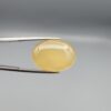 Multi-angle macro photographs of a 19.18-carat natural yellow chalcedony agate (Zard Aqeeq) oval cabochon from Iran held in metal tweezers, showcasing a smooth, domed surface, uniform honey-yellow translucency, and a high-gloss finish.