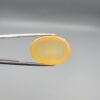 Multi-angle macro photographs of a 19.18-carat natural yellow chalcedony agate (Zard Aqeeq) oval cabochon from Iran held in metal tweezers, showcasing a smooth, domed surface, uniform honey-yellow translucency, and a high-gloss finish.