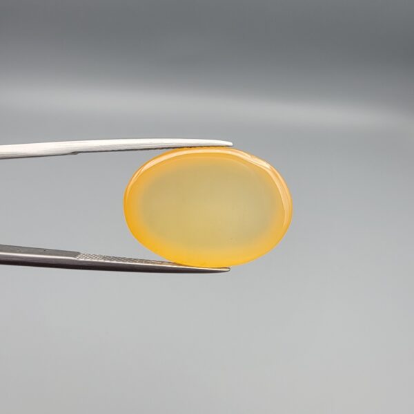 Multi-angle macro photographs of a 19.18-carat natural yellow chalcedony agate (Zard Aqeeq) oval cabochon from Iran held in metal tweezers, showcasing a smooth, domed surface, uniform honey-yellow translucency, and a high-gloss finish.