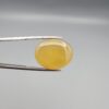 Multi-angle macro photographs of a 19.61-carat natural yellow chalcedony agate (Zard Aqeeq) oval cabochon from Iran held in metal tweezers, highlighting a smooth domed profile, uniform honey-yellow translucency, and a high-gloss reflective surface.
